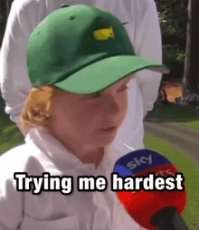a young boy wearing a green hat is talking into a microphone with the words trying me hardest written below him