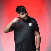 a man wearing a black adidas shirt stands in front of a red wall