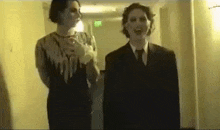 two people in suits are standing next to each other in a hallway and laughing .