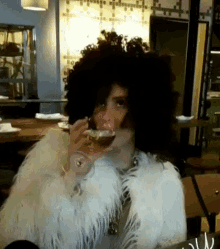 a woman with a large afro is drinking a glass of wine in a restaurant