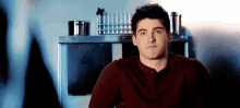 a young man in a red shirt is sitting in front of a microwave .