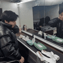 a man in a leather jacket is looking at himself in a mirror with wipes on the counter