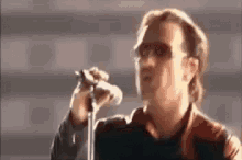 a man is singing into a microphone while wearing sunglasses and a leather jacket .