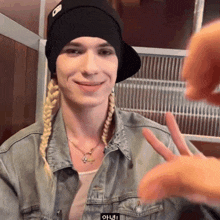 a woman wearing a denim jacket and a black hat with the letter o on it is smiling and making a peace sign