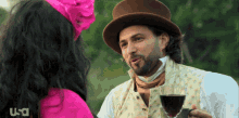 a man in a top hat is holding a glass of wine and talking to a woman in a pink dress