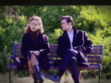 a man and a woman sit on a park bench talking to each other