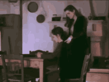 a woman is standing next to another woman who is sitting at a table in a dark room