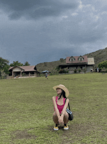 a woman in a straw hat is squatting in a field