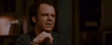 a man is sitting at a table talking to another man while holding a cell phone .
