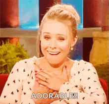 a woman is smiling and holding her hands to her chest while saying `` adorable '' .