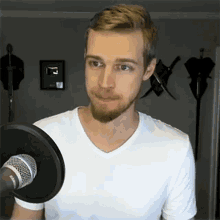 a man with a beard is standing in front of a microphone with a picture on the wall that says " i "