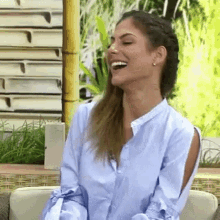 a woman in a blue shirt is laughing and sitting in a chair .