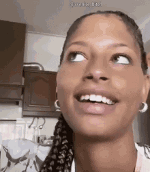 a close up of a woman 's face with braids and earrings smiling in a kitchen .