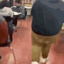 a group of people are sitting at desks in a classroom and a man is walking through the hallway .