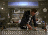 a man in a suit stands in front of a row of shot glasses in a lab
