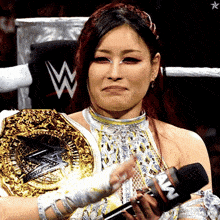 a woman in a wrestling ring is holding a microphone and wearing a wrestling belt