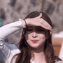 a woman in a white sweater is covering her eyes with her hand .