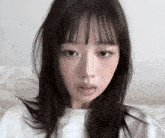 a woman with long black hair and bangs is wearing a white shirt .