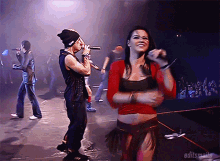 a woman in a red top is singing into a microphone while a man in a beanie sings into a microphone