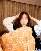 a girl sitting on a couch with her hands on her head