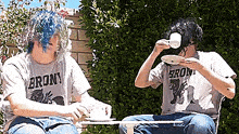 two men wearing brony shirts sit at a table drinking tea