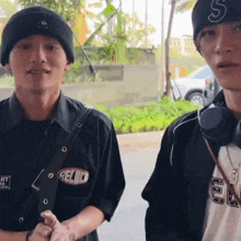 two young men wearing beanies and headphones are standing next to each other on a street .