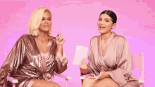 two women are talking to each other on a pink background .