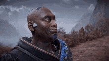 a man with a triangle on his forehead is smiling in front of mountains