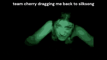 a green image of a woman in a dark room with the words `` team cherry dragging me back to silksong '' written on it .