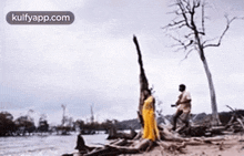 a man and a woman are standing on a beach next to a river .