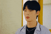 a young man wearing a white shirt and a black necklace is making a funny face