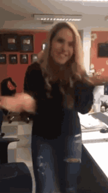 a woman in a black shirt and ripped jeans is dancing in a room .