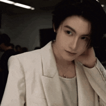 a young man wearing a white jacket and a white shirt is adjusting his hair .