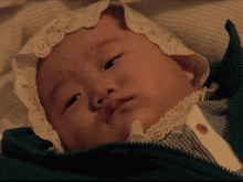 a baby wearing a white lace bonnet is laying in a green jacket