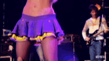 a woman in a purple skirt is dancing on a stage with a man playing a guitar