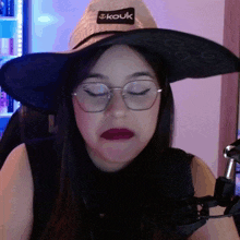 a woman wearing a witch hat and glasses has a label on her hat that says " kouk "