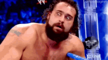 a man with a beard is wrestling in a ring with a blue rope .