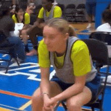 a woman in a yellow shirt sits in a chair on a basketball court .