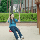 a woman in a blue shirt is sitting on a swing in a playground