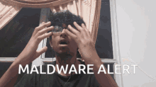 a man wearing glasses covering his eyes with his hands and the words maldware alert behind him