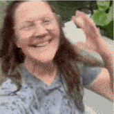 a woman wearing glasses and a blue shirt is smiling and waving her hands .