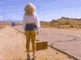 a woman is standing on the side of the road holding a suitcase and waving