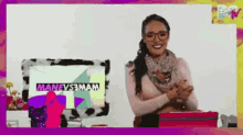 a woman wearing glasses and a scarf is smiling in front of a computer screen that says manevs3mam