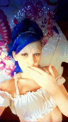 a woman with blue hair and a white top covering her mouth with her hand