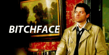 a man in a trench coat and tie is standing in front of a framed picture that says bitchface