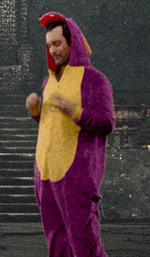 a man in a purple and yellow dinosaur costume making a heart shape with his hands