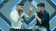 two men singing into microphones with the letters rtve on the bottom right