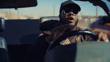 a man wearing sunglasses and a ferrari shirt is driving a car
