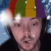 a man wearing a colorful hat and headphones is looking at the camera with snow falling in the background .