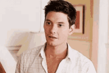 a man in a white shirt is standing in a living room looking at something .